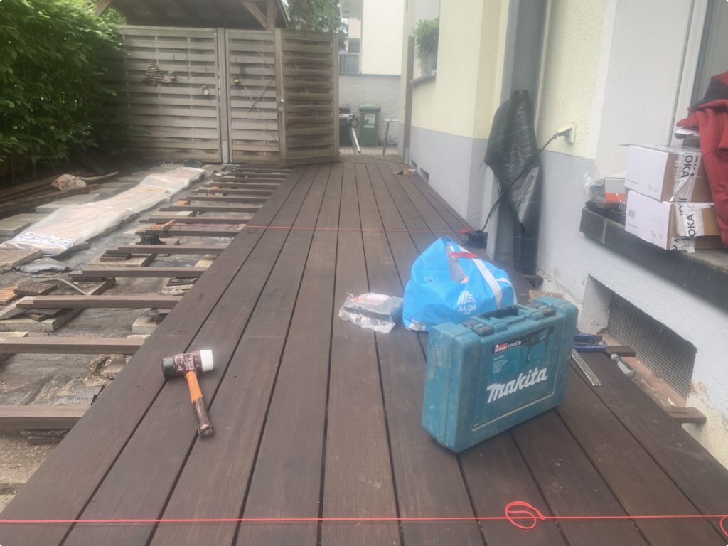 Bau einer neuen Bambusterrasse in Frankfurt-Bornheim. Die ersten dunkelbraunen Terrassendielen werden auf der Unterkonstruktion verlegt und mit einer Richtschnur exakt ausgerichtet.