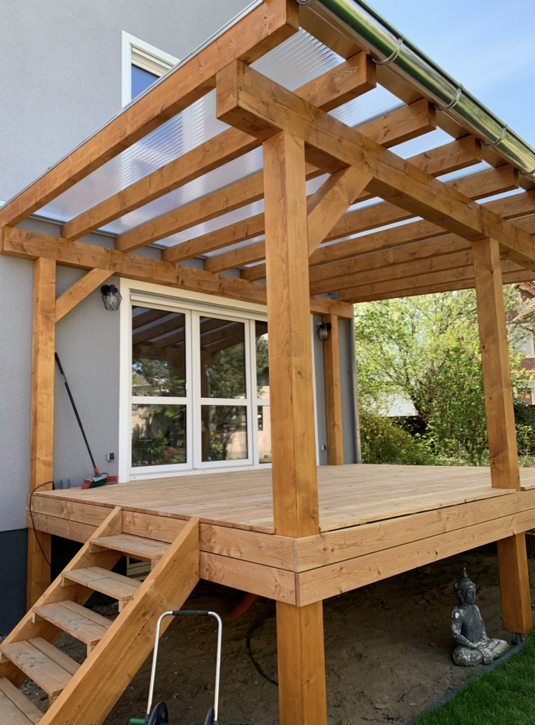 Fertiggestellte Holzterrasse aus Douglasie mit maßgefertigter Terrassenüberdachung.